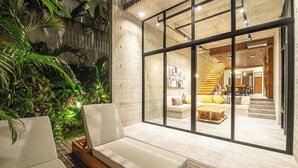 A modern interior with a glass wall, a wooden staircase, and a cozy seating area with cushions.
