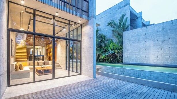 A modern building with large glass windows, a wooden deck, and a concrete wall with greenery. - Robyn s Villa New Modern 4 BR Villa Canggu (Kerobokan)