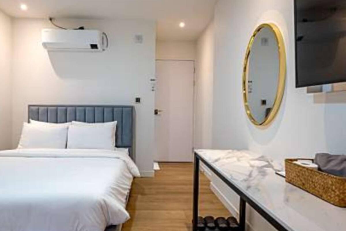 A bedroom with a bed, a bedside table, a mirror, and an air conditioning unit.