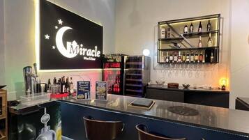 A bar area with a neon sign reading "Miracle Wine & Beer," a selection of bottles on shelves, and a counter with a digital scale.