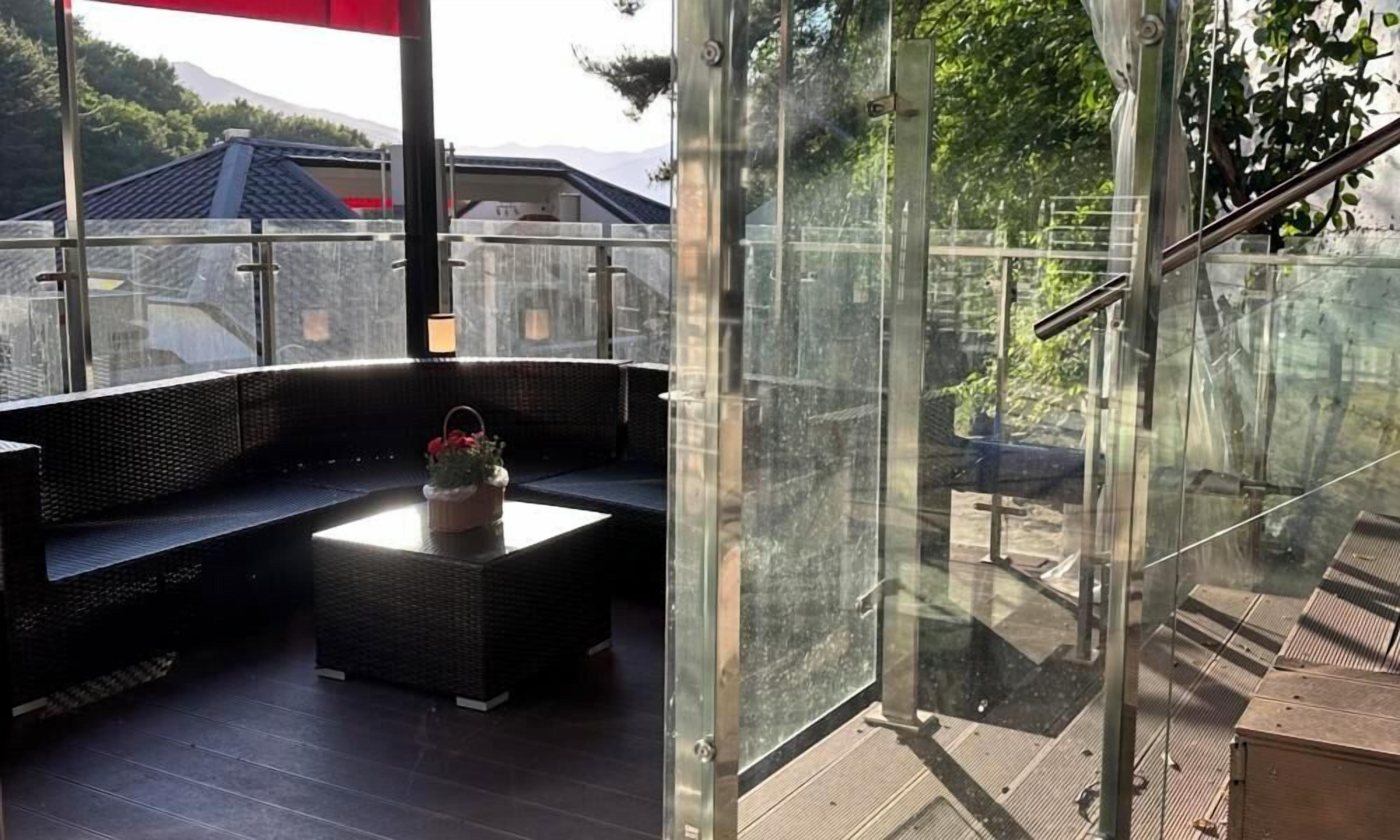 A modern outdoor seating area with a glass partition, a cushioned bench, and a small table with a flower arrangement.