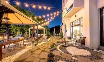 Área de pátio externa com luzes de corda, assentos e plantas em vasos.