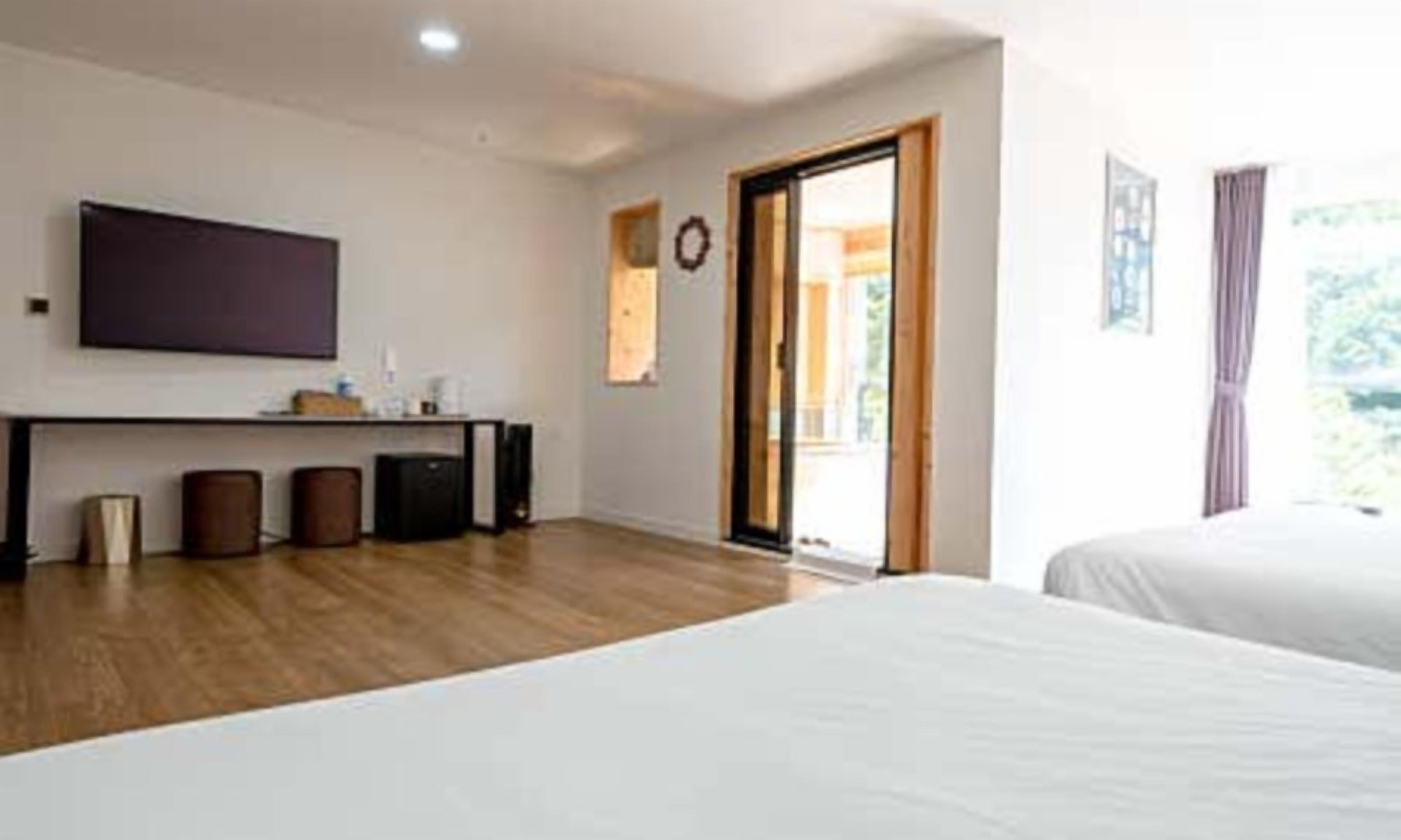A hotel room with a bed, a desk with a computer, a TV, and a sliding glass door to the outside.