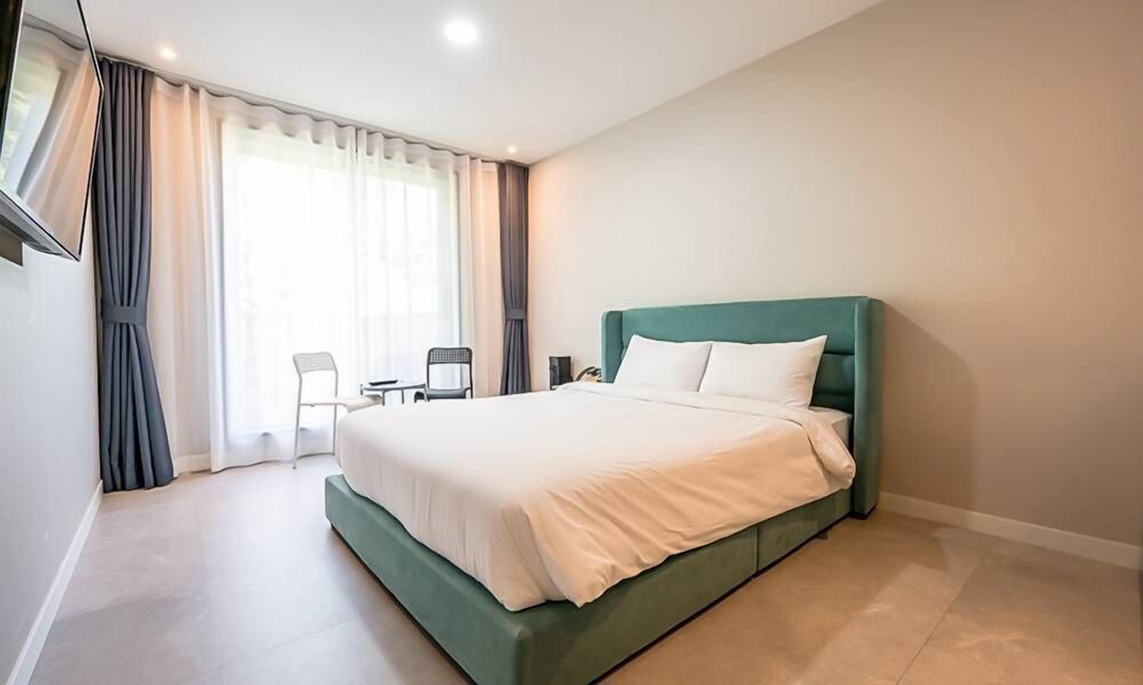 Habitación de hotel con una cama grande, una mesita pequeña con dos sillas y un televisor montado en la pared.