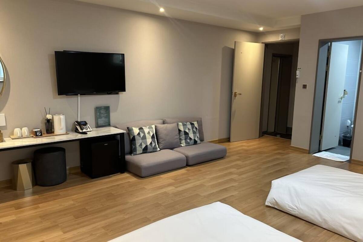 A modern hotel room with a flat-screen TV, a desk with a telephone, a sofa, and a bed.