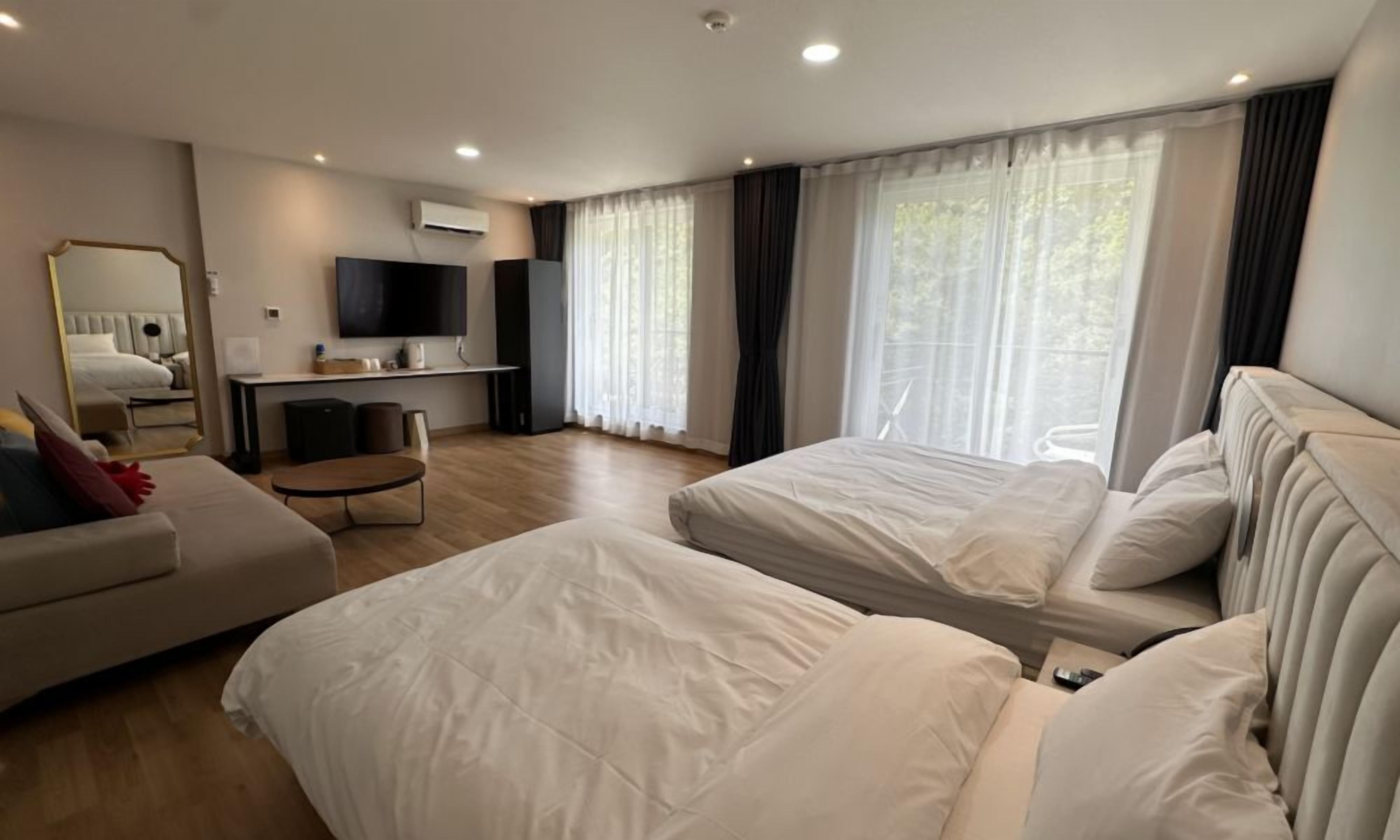 Moderni hotellihuone, jossa on kaksi sänkyä, sohva, televisio ja työpöytä.