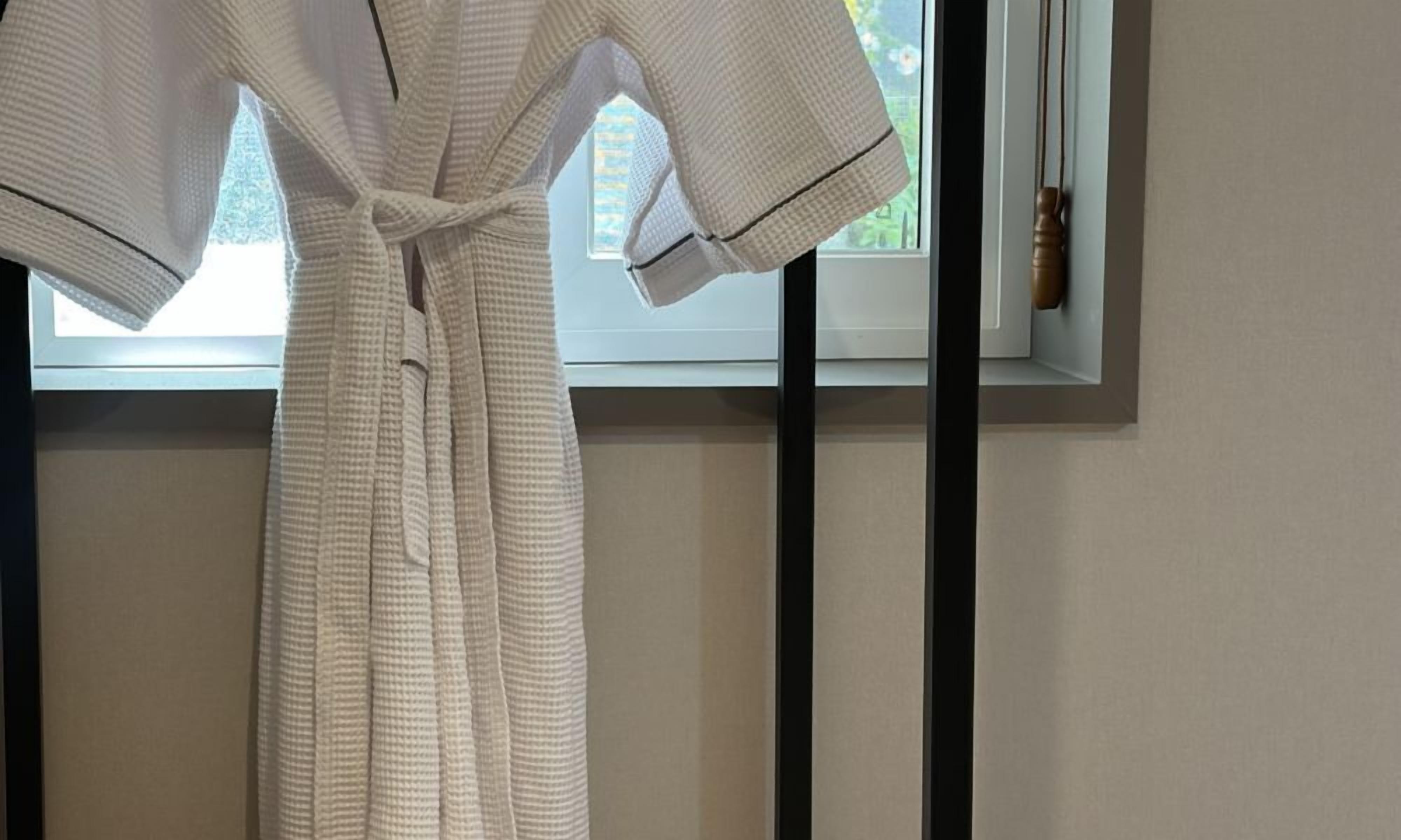 A white bathrobe hanging on a hook near a window with a view of the outdoors.