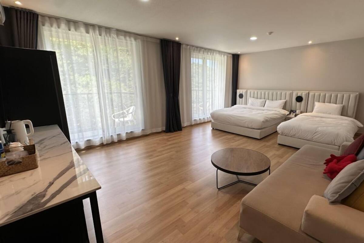 A modern hotel room with two beds, a sofa, a coffee table, and a TV.
