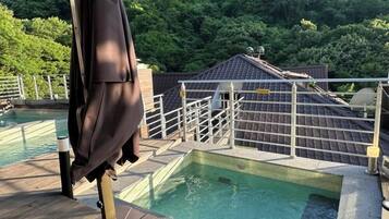 A swimming pool with a wooden deck, surrounded by a metal railing and a view of a forested area.