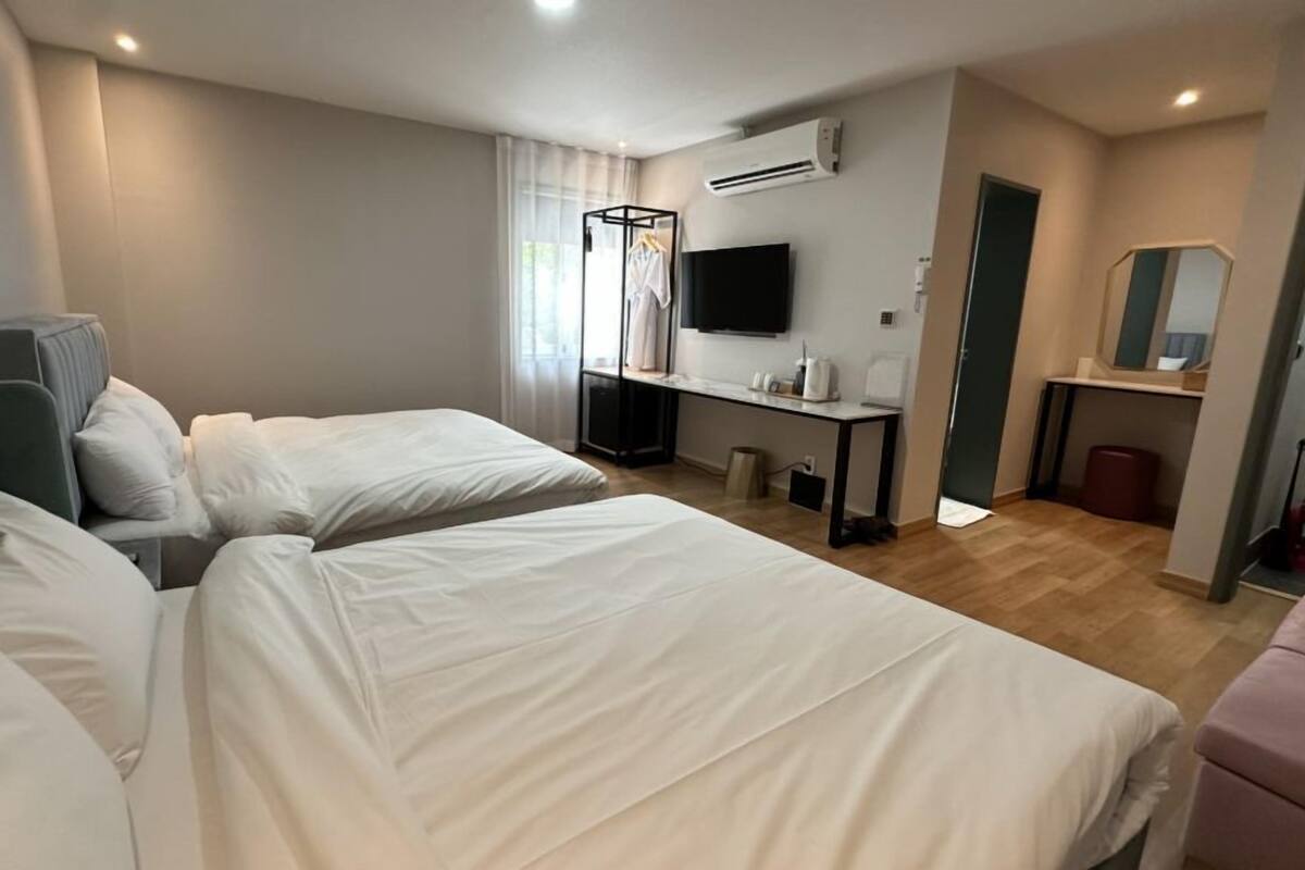 A hotel room with two beds, a desk, a TV, and a mirror.