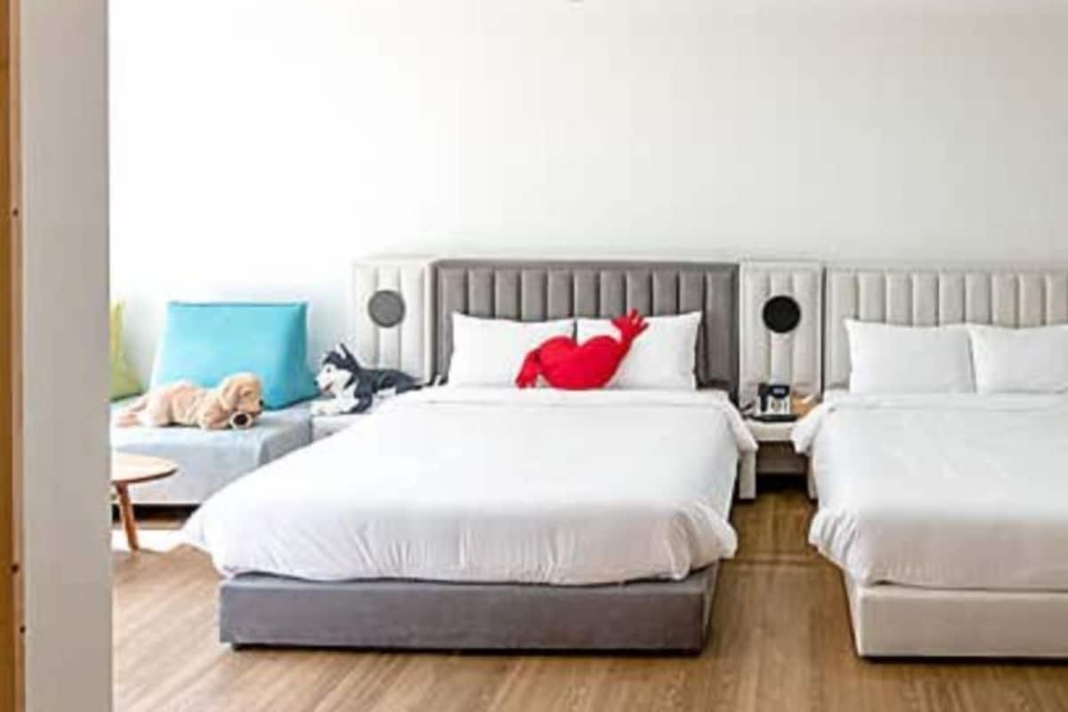 A hotel room with two beds, a grey headboard, and a small bedside table with a lamp.