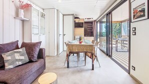 A modern interior with a sofa, dining table, and a view through large windows. - Chalet moderne La Baule-Guérande by Interhome (Guérande)