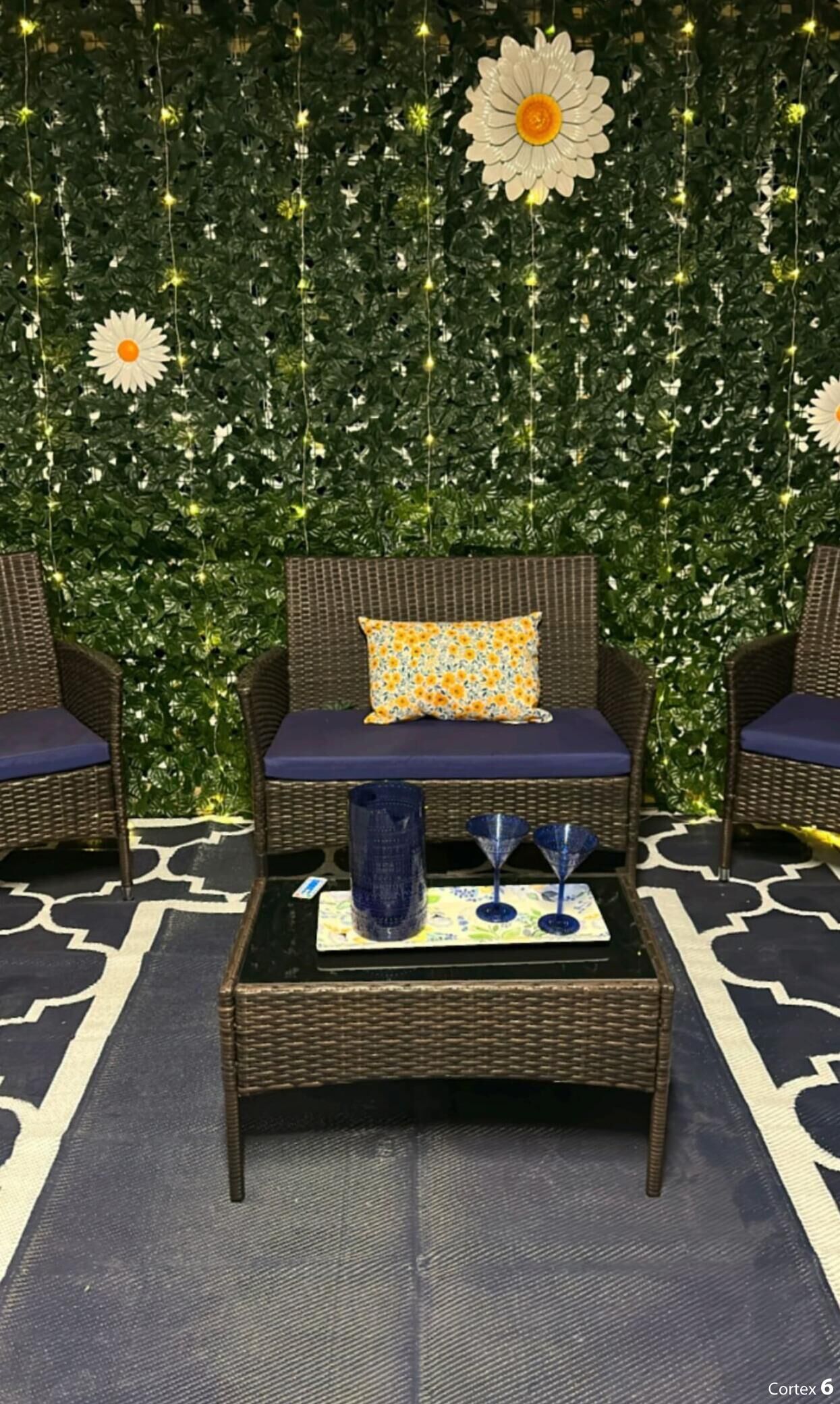 Una habitación con muebles de mimbre, un tapiz estampado y una pared decorada con plantas y luces de cadena.