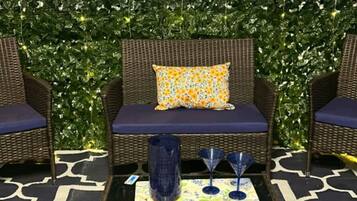 Una habitación con muebles de mimbre, un tapiz estampado y una pared decorada con plantas y luces de cadena.