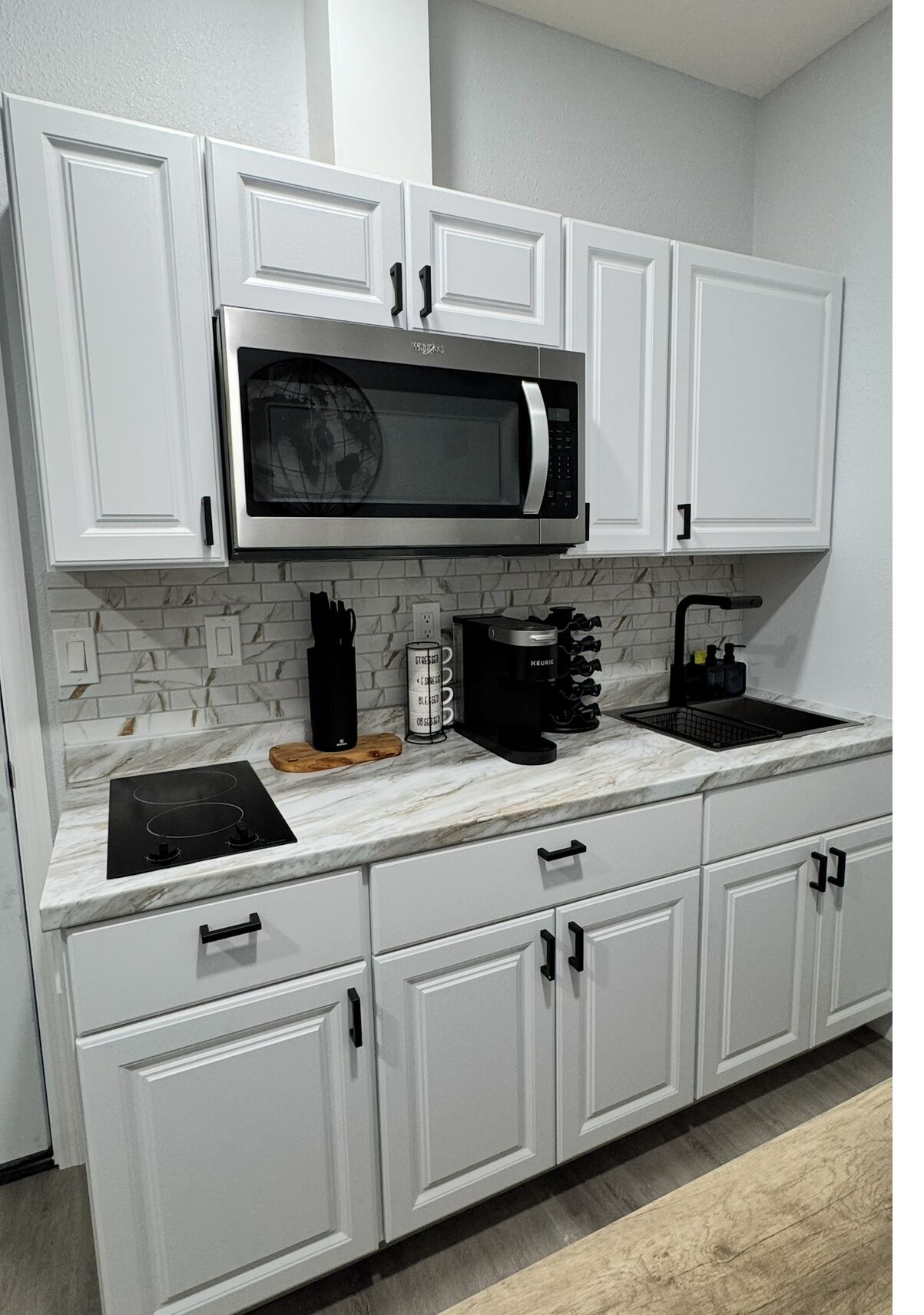 A modern kitchen with white cabinets, a built-in microwave, a coffee maker, and a gas stove.