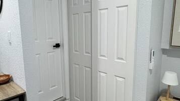 A hallway with a white door, a small table with a bowl, and a lamp on a wooden side table.