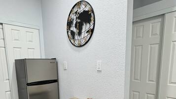 Una cocina con una mesa de madera, sillas negras, un refrigerador de acero inoxidable y un cuadro con un mapa del mundo en la pared.
