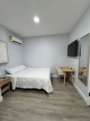 A bedroom with a bed, a desk, a chair, a TV, and an air conditioning unit. - Cozy studio in charming Riverview (Riverview)