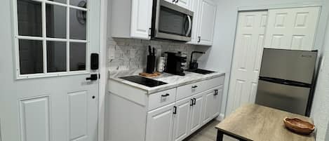 A compact kitchen with white cabinetry, a microwave, a refrigerator, and a dining table with a bench.