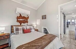 Une chambre dotée d’un grand lit, d’un climatiseur fixé au mur, d’une œuvre d’art représentant une carte et donnant sur la pièce adjacente.
