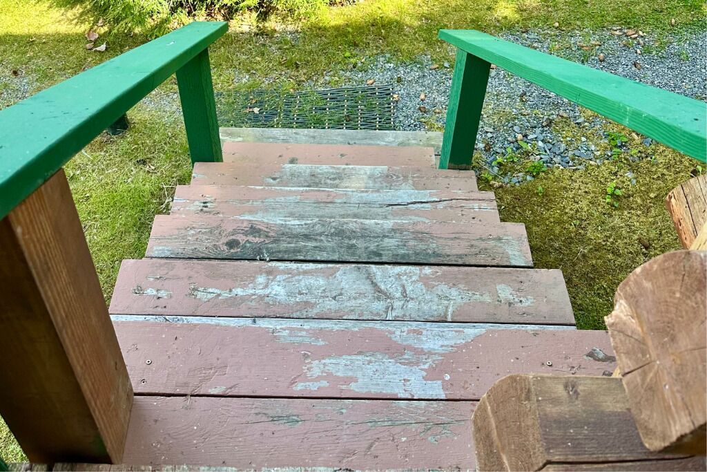 Una escalera de madera con barandillas verdes que da a una zona cubierta de césped.