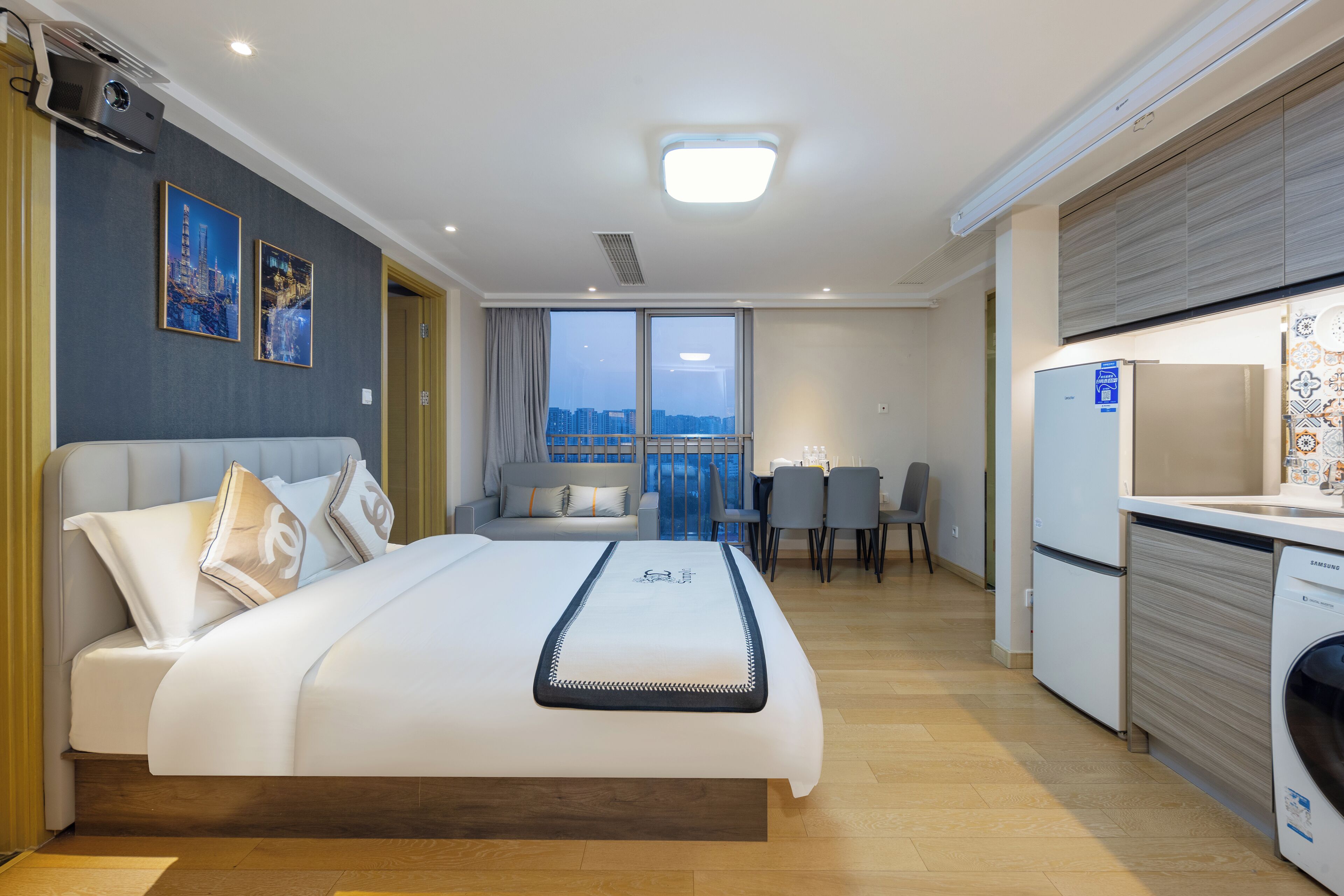 A modern hotel room with a large bed, a dining area, and a kitchen.