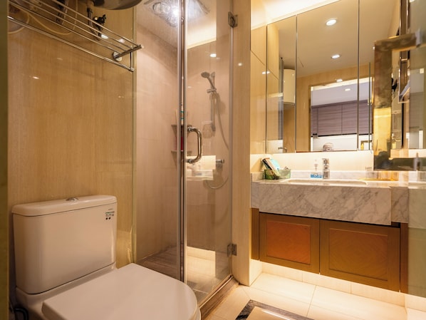 Un baño moderno con cabina de ducha de vidrio, inodoro blanco y encimera de mármol con lavabo y espejo.
