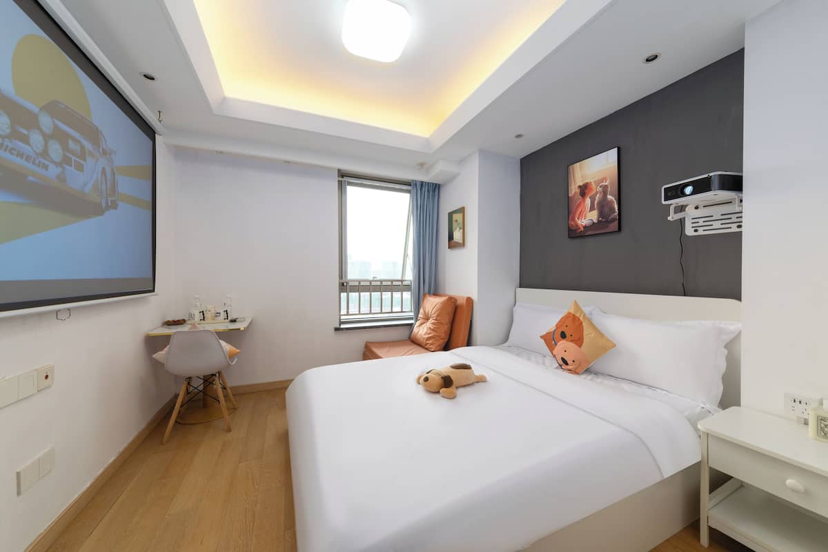 Une chambre d’hôtel moderne équipée d’un grand lit, d’un bureau et d’un écran de projection.