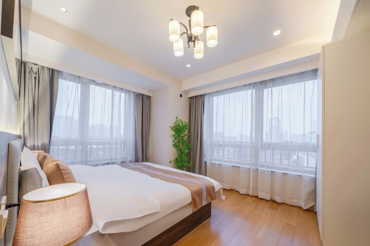 Une chambre d’hôtel moderne avec un grand lit, une lampe de chevet et une vue sur la ville grâce à de grandes fenêtres.