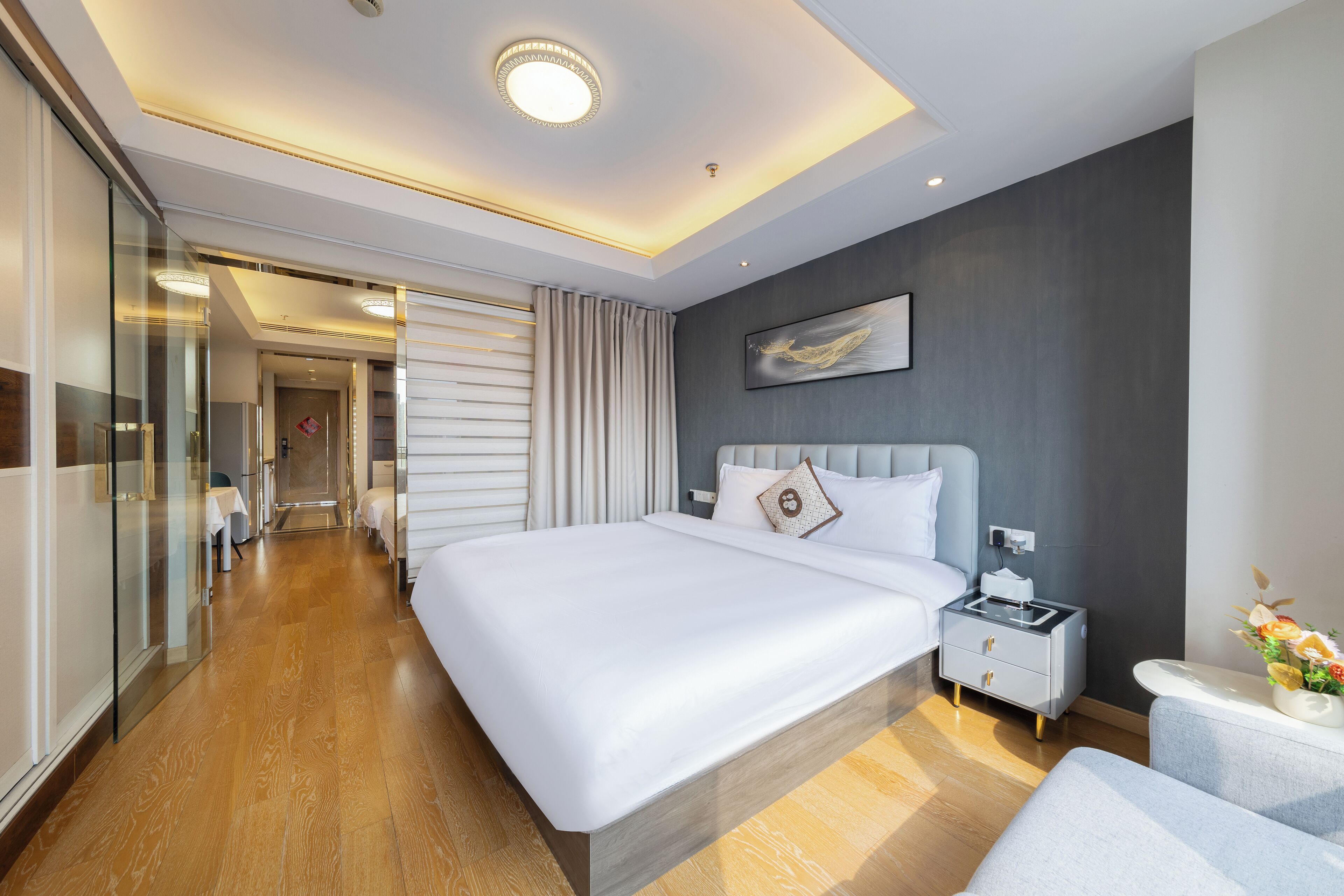 A modern hotel room with a large bed, bedside tables, a nightstand, and a glass partition.