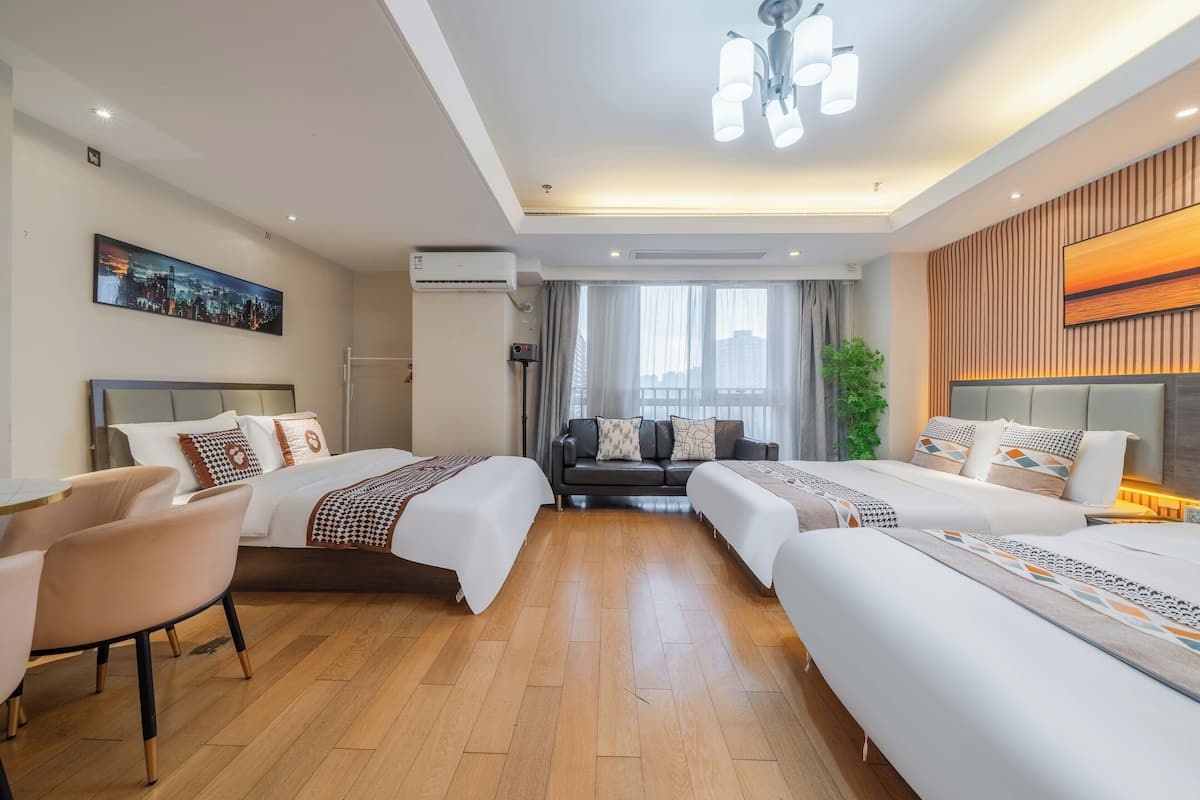 Une chambre d’hôtel avec deux lits, un canapé, un fauteuil, une grande fenêtre avec des rideaux, un tableau représentant un paysage urbain, un appareil de climatisation et un luminaire au plafond.