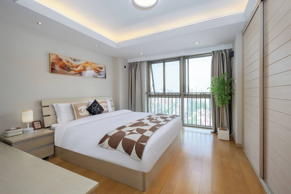 Une chambre d’hôtel moderne avec un grand lit, une table de chevet, une commode, une fenêtre avec des rideaux et une vue sur la ville.