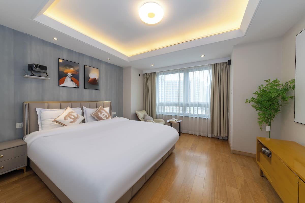 Une chambre d’hôtel moderne avec un grand lit, un petit bureau, une plante et une fenêtre avec des rideaux.
