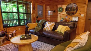 Ein gemütliches Cabin-Interieur mit Ledersofa, rundem Holztisch und einem grünen Couchsofa.
