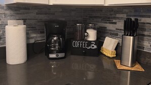 A kitchen with white cabinets, a coffee maker, a paper towel holder, and a knife block on the counter.