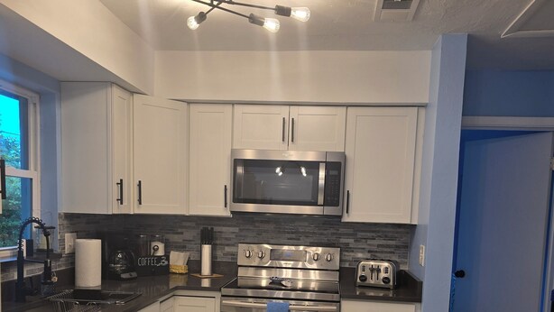 A modern kitchen with white cabinets, a stainless steel microwave, an oven, and a coffee maker.