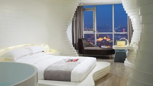 Une chambre d’hôtel moderne dotée d’un grand lit, d’un coin salon et offrant une vue sur la ville la nuit.