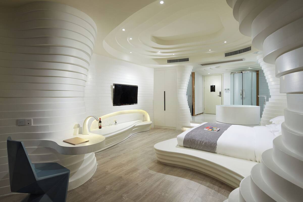 Een moderne slaapkamer met een gebogen bed, een inbouw bureau en een flatscreen televisie.