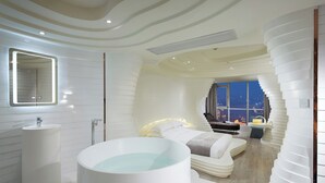 Une salle de bain moderne avec une grande baignoire, un lavabo et un miroir. Une fenêtre offre une vue sur la ville la nuit.