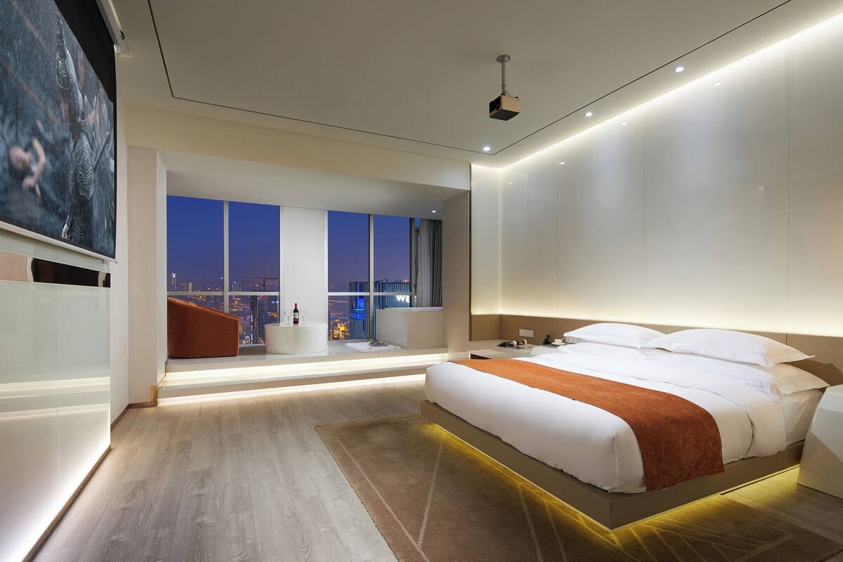 Een moderne hotelkamer met een groot bed, een zithoek met uitzicht en een stadsbeeld door de ramen.