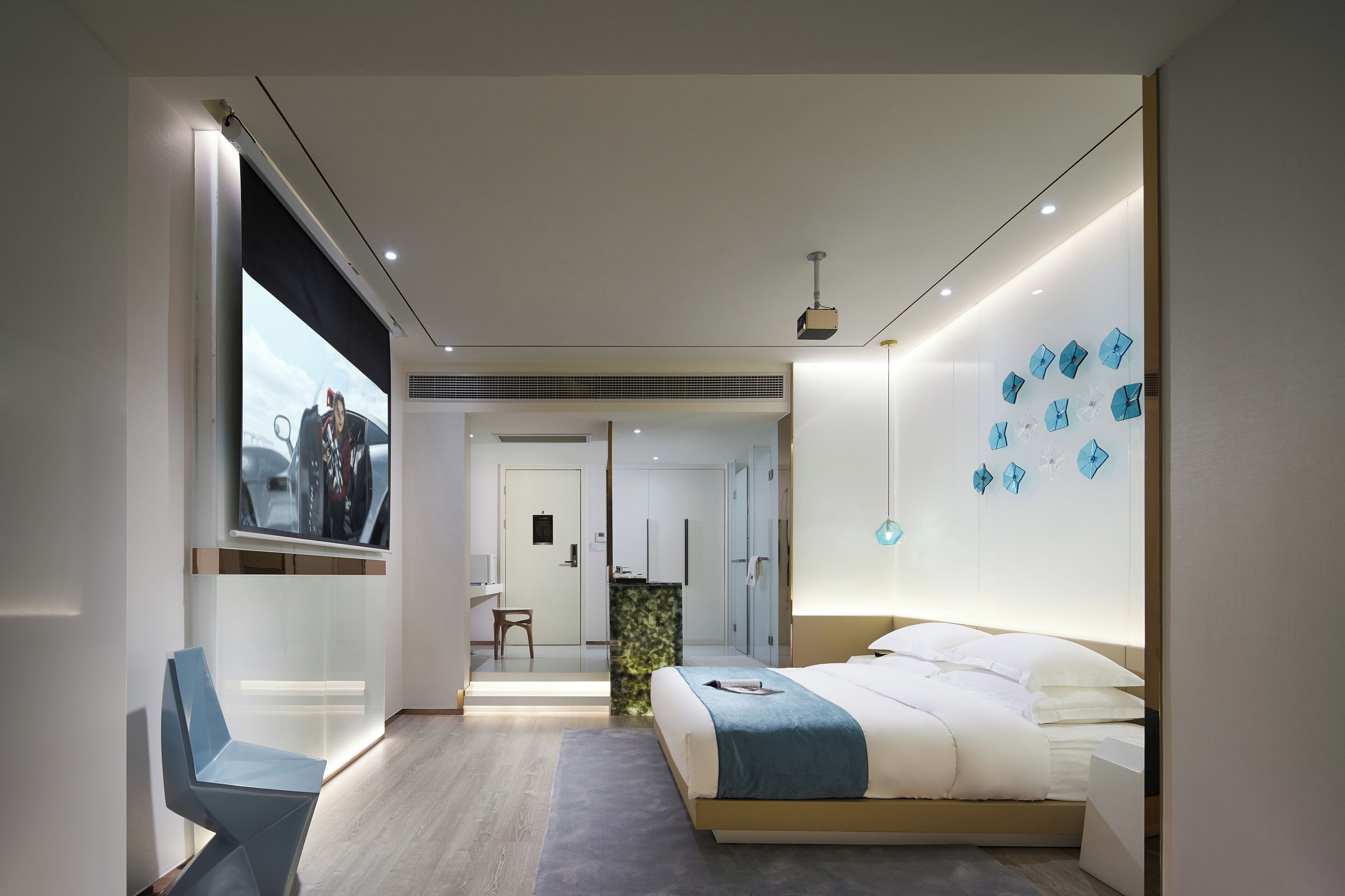 Ein modernes Hotelzimmer mit Bett, Schreibtisch und Stuhl. Ein großes Fenster und eine Wand mit dekorativen Elementen sind ebenfalls vorhanden.