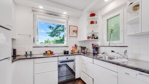 A modern kitchen with white cabinetry, a built-in dishwasher, and a window providing a view of greenery outside.