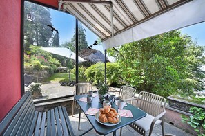 Un patio exterior con una mesa dispuesta para dos personas, un banco y vistas a un jardín.