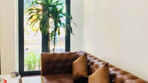 Un salon avec un canapé en cuir marron, une grande fenêtre donnant sur un paysage verdoyant et un tableau accroché au mur.