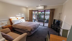 A hotel room with a bed, a sofa, a TV, and a balcony with a view of the outside. - Alpine Springs Motel | Unit 5 - HS31215 (Hanmer Springs)