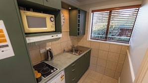A compact kitchen with a microwave, stove, sink, and green cabinets. - Alpine Springs Motel | Unit 5 - HS31215 (Hanmer Springs)