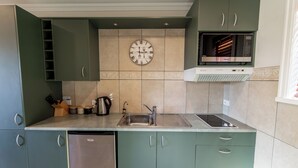 Een keuken met groene kastjes, een roestvrijstalen spoelbak, een klok en een magnetron.
