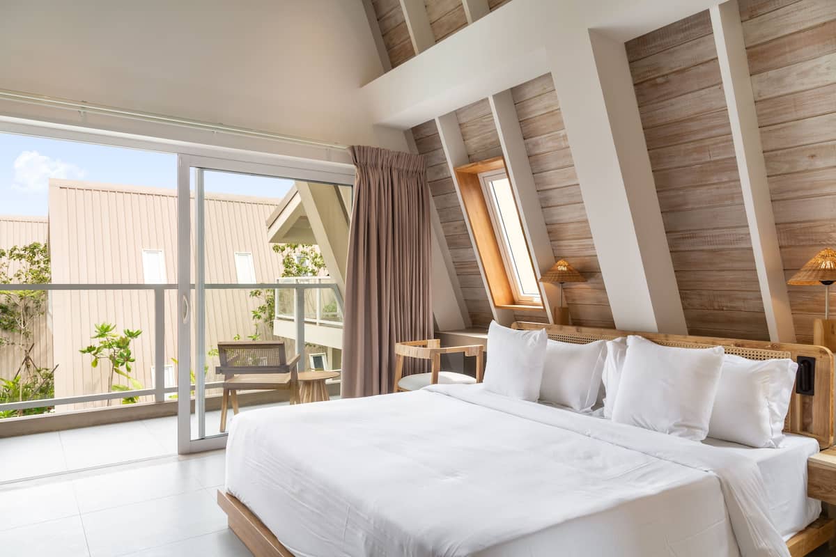 Une chambre dotée d’un grand lit, d’un plafond en bois et d’une porte-fenêtre coulissante donnant sur un espace extérieur agrémenté de plantes.