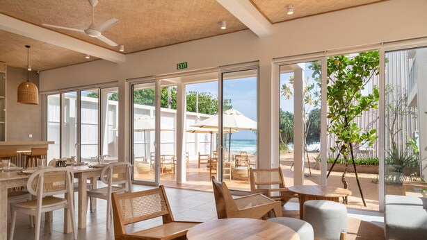A spacious indoor area with large windows, wooden furniture, and a view of the beach. - Asaya Sands (Mirissa)