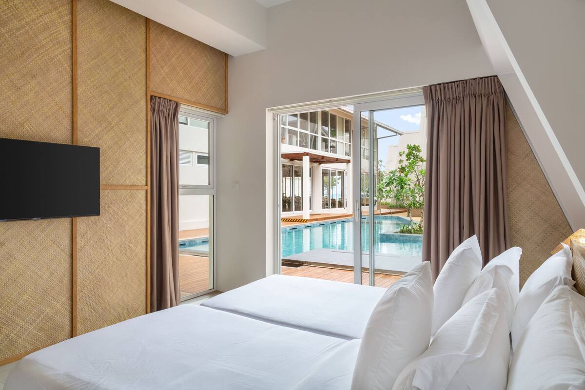 Une chambre d’hôtel avec un lit, une télévision et une porte-fenêtre coulissante donnant sur une zone avec piscine.